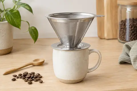 Filtre à café conique en inox à double couche posé sur une tasse en céramique claire