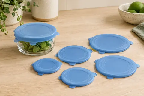 Six petits couvercles extensibles bleus en silicone, dont un posé sur un récipient en verre.