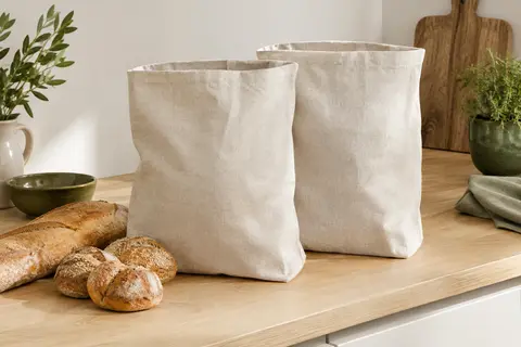Deux sacs à pain en lin naturel posés près d’une baguette et de petits pains sur un plan de travail