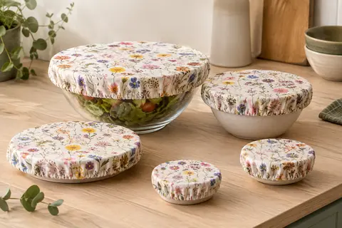 Cinq couvre-plats en tissu à motifs floraux, posés près d’un bol en verre dans une cuisine lumineuse.