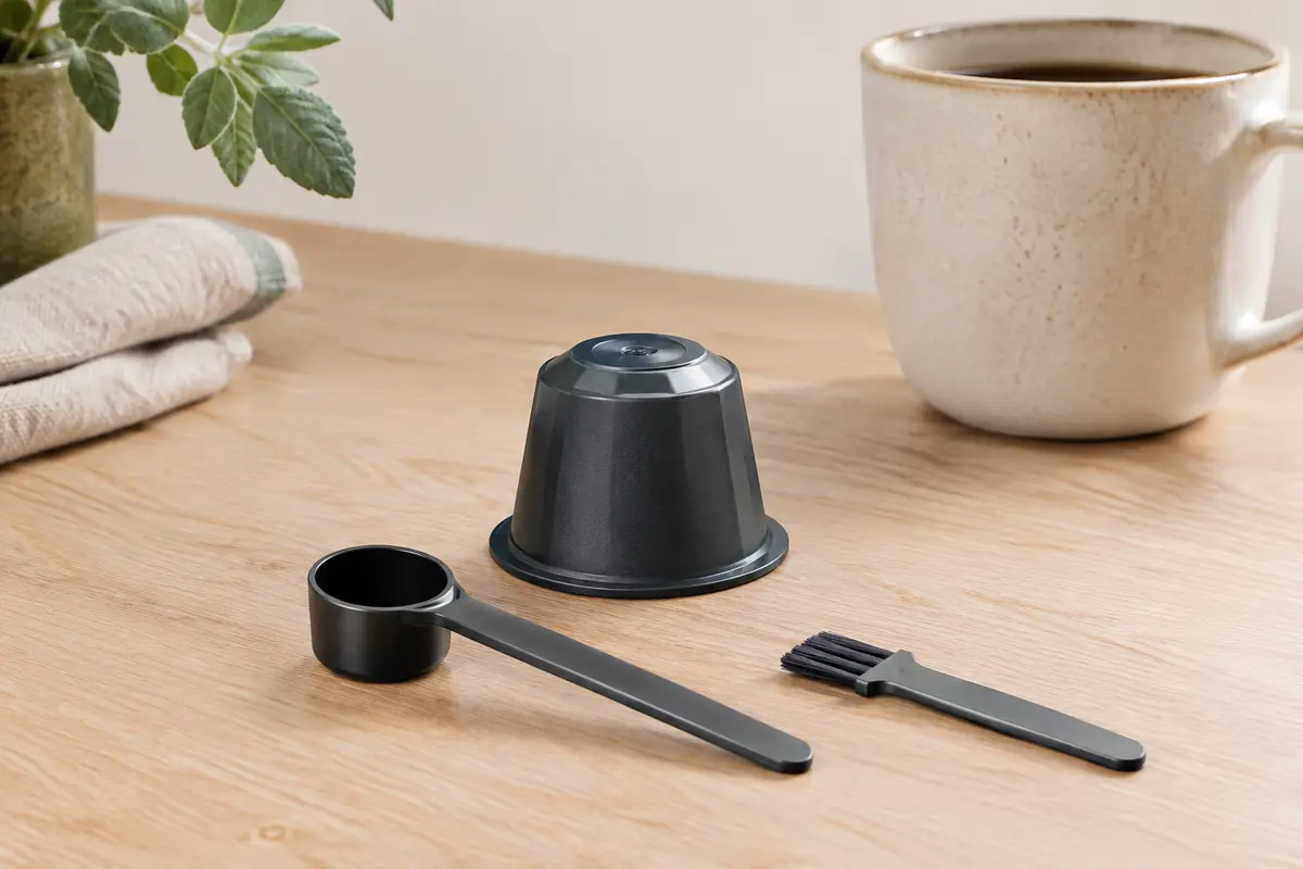 Capsule de café rechargeable en plastique PP avec sa cuillère et son pinceau sur un plan de travail.