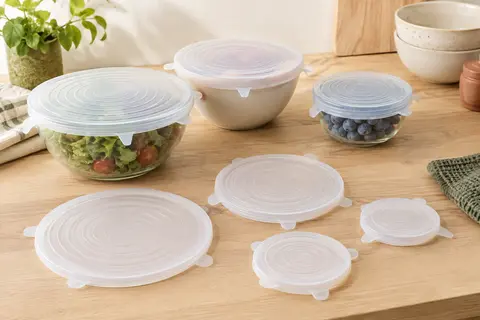 Six couvercles extensibles en silicone blanc de tailles variées, disposés près de bols dans une cuisine lumineuse.