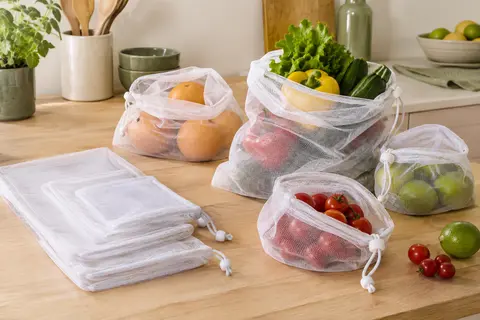 Sacs en filet blancs à cordon, de plusieurs formats, posés près de fruits et légumes sur un plan de travail.